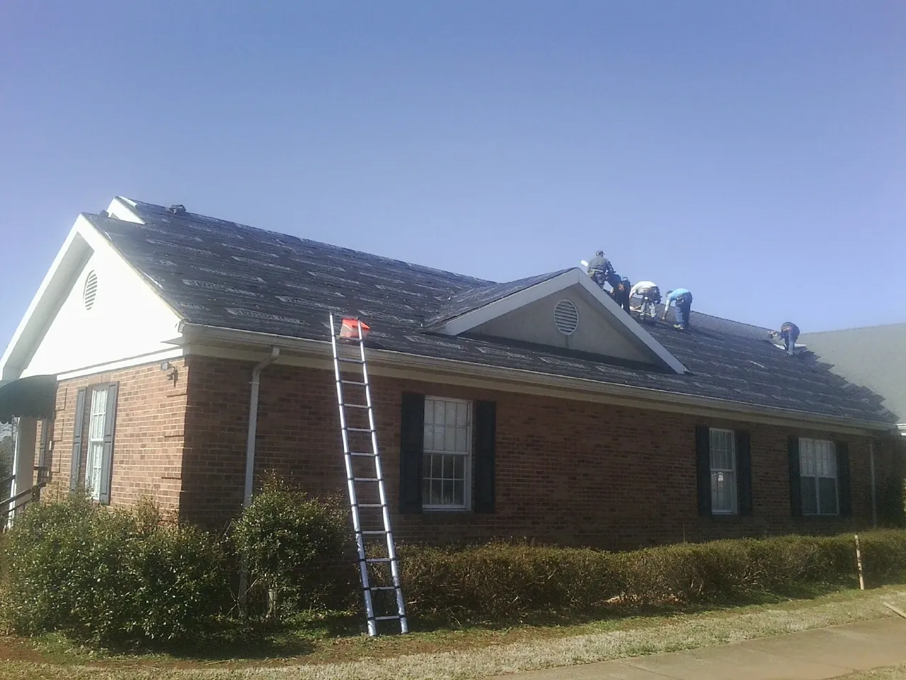 Crew tearing shingles off a brick ranch roof with a ladder set — Emergency Roof Repair work by our crew in Girard