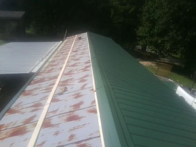 Old rusted panels beside newly installed green metal roofing — Wind Damage Roof Repair by Roofing Brothers in Girard