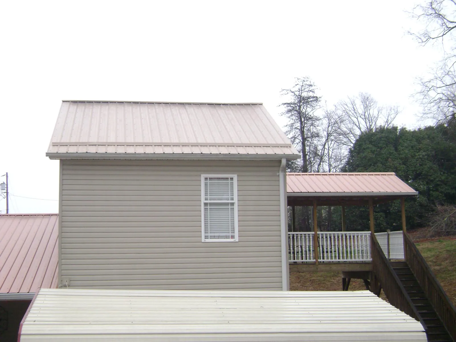 Tan metal roofs on a two story addition and attached porch, from a Roof Replacement job in Girard
